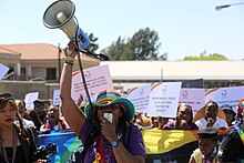 A person wearing a rainbow hat at Soweto Pride 2023 parade holding up a Megaphone and speaks into it.