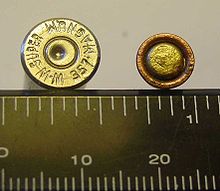 A fired pistol case as indicated by the dimple from a firing pin and a shotgun (right) primer against an inch and mm scale. Pistol and shotgun primers.jpg