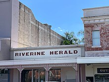 Riverine Herald sign across building between two taller buildings