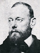 head and shoulders portrait of a middle-aged man with a beard wearing a striped jacket