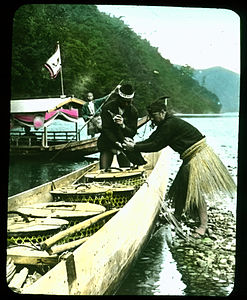 Two boats on river, a passenger boat being poled and a fishing boat filled with lidded open work baskets