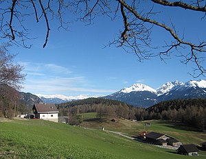 Vue depuis le plateau de Seefeld au sud-est jusqu'au Zirler Berg boisé (centre) ;  devant elle, entre les maisons, la colonne de peste de Leithen ;  au fond à droite la Marchreisenspitze, à gauche la Saile;  à gauche à l'horizon les Alpes de Tux