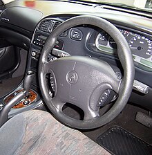 VX II Berlina interior displaying steering wheel command controls and a wood grain-faced transmission selection lever. 2001-2002 Holden Berlina (VX II) sedan (2007-05-07).jpg