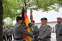 Ein Offizier übergibt eine schwarz-rot-goldene Fahne an einen anderen Offizier.