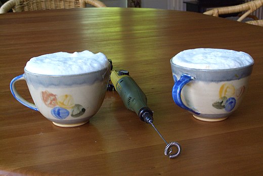 Twee koppen cappuccino met een elektrische melkklopper