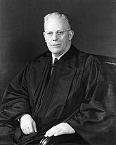 A formal portrait of a judge, in his robes, sitting.
