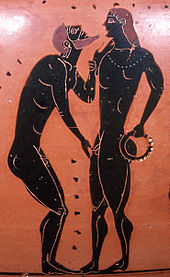 Darstellung auf einer römischen Amphore aus dem Jahre 540 vor Christus: zwei schlanke, muskulöse, nackte Männer stehen sich gegenüber, der linke berührt Kinn und Penis des rechten.