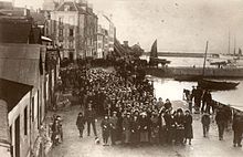 Foule de personnes massée le long d’un petit port maritime.