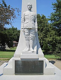 Гранитна статуя на млад войник във военна униформа, стоящ пред обелиск на върха на плоча, описваща постиженията му
