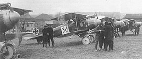 Photo noir et blanc d'avions biplans stationnés devant des hangars avec des groupes d'hommes discutant entre eux devant les appareils