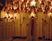 "לוסיה" עם "כתר האור", ומאחוריה הבנים חבושי הכובעים ומחזיקי השרביטים, והבנות אוחזות הנרות, בעת שירת שירי החג