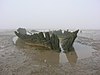 Hulk di legno della nave, circondato da sabbia bagnata.