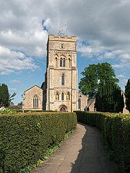 English: St. Peter's Church, Brackley, in 2023. View from a western direction in afternoon light, with hedges in the foreground lining the path to the main entrance.