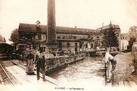 Vista de una fábrica y su chimenea junto a un arroyo en una postal del siglo XX.