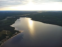 An aerial shot of Faillon Lake with the sun shining on it from low in the sky.