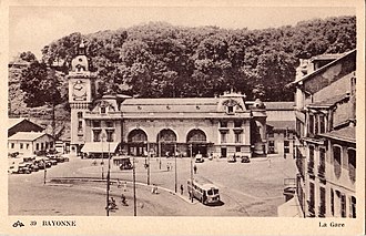 Carte postale sépia représentant la vue extérieure d’une gare.