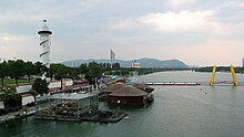 Copa Cagrana with lighthouse and pontoon bridge, from SE. In the background: Millennium Tower, Kahlenberg (w. antenna), Leopoldsberg (w. church) and, far out, Klosterneuburg.