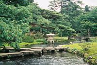 Een Japanse tuin met water, brug en lantaarn