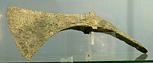 Verdigrised pickaxe. The bottom edges of the axe blade and the pick form one continuous curve. The top of the axe is also mildly concave between the eye and the blade. The sharp edge of the blade curves from nearly parellel to the (missing) handle to nearly at 45 degreees to it.