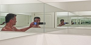 Man photographing himself in cornered mirror to generate illusion cropped.jpg
