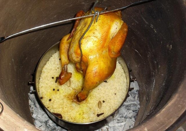 A whole chicken suspended above rice and charcoal.
