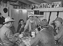 Muskrat trappers in Delacroix, Louisiana, 1941, gathered around a large bottle of "Cream of California - California Claret", an early Gallo mass-produced wine Muskrat trappers drinking wine and playing cache, Delacroix Louisiana, 1941 crop.jpg