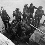 nine British soldiers and one sailor on a small boat at sea. A Union Jack flies from a mast at the rear.