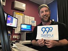SWR 99.9 FM's breakfast announcer, Busco, holding the new logo SWR Triple 9 Rebrand.jpg