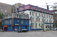 Three-storey building in the foreground painted royal blue and grey, with a four-storey building in the background painted white and pink