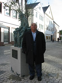 יצחק בלפר ליד האנדרטה לזכר קורצ'אק והילדים אותה יצר בגינזבורג, גרמניה, 2003