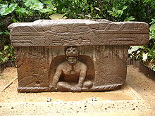 Altar 4 at La Venta. Note the rope that winds along the ground, held by the figure. Note also the eyes and the fangs on the cornice above the figure, implying that the figure is seated in that creature's mouth. (For an oblique view of Altar 4, click here.) Altar 4 La Venta (Ruben Charles).jpg