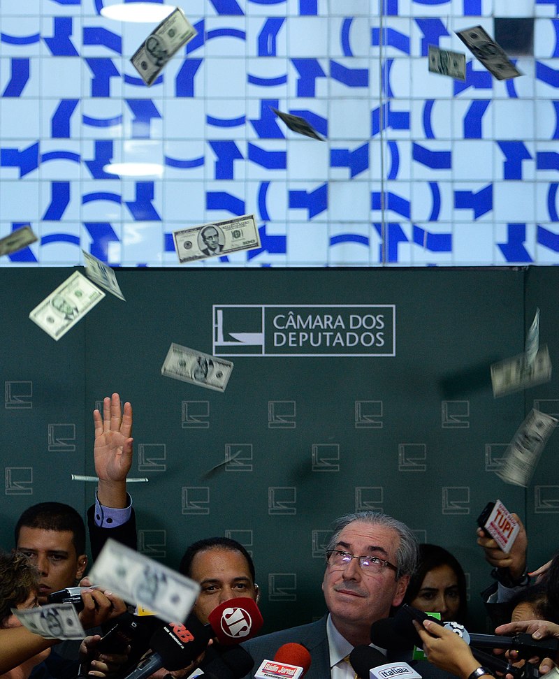 Imagem mostra Eduardo Cunha, Ã  Ã©poca presidente da CÃ¢mara dos Deputados, recebendo banho de dÃ³lares falsos contendo o seu rosto em forma de protesto contra a corrupÃ§Ã£o.