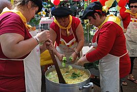 Photo montrant trois femmes habillées en rouge et portant un foulard jaune préparant un plat.