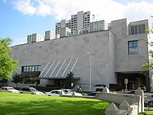 Bâtiment trapu en béton avec grand passage sous aile.  Un toit pour l'entrée est attaché au bâtiment par des poteaux coudés.