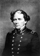 Photograph of a man, seated, with balded head, wild hair, in double-breasted naval uniform