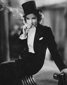 Marlene Dietrich in the 1930 film Morocco, wearing her signature masculine attire, featuring a white tie and top hat.
