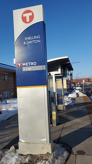 A bus shelter with a tall sign with the station name