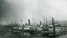 Olympian and Alaskan (steamers with schooner rigs, tall chimneys and walking beams) laid up in Portland, Oregon sometime before May 1889, at the OR&N steamboat boneyard. Steamboat boneyard Willamette River circa 1885.jpg