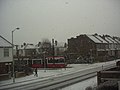 A tram is pulling out of Addiscombe Tram stop in a short snow frenzy.