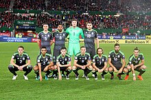 A football team line-up with four players standing behind seven kneeling players.