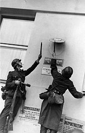 Photo de deux soldats allemands retirant les insignes du gouvernement polonais d'un mur.