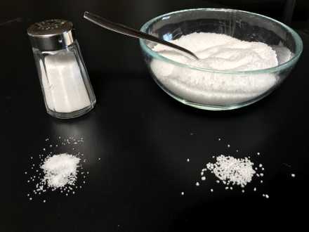 Comparison of table salt with kitchen salt. Shows a typical salt shaker and salt bowl with salt spread before each on a black background.