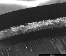 A side profile of an Easton Carbon One arrow with a spine of 900, taken with a scanning electron microscope (SEM). The arrow is a bond of two carbon tubes, an inner and an outer tube (black wires). In between both carbon layers, another fiber is used (white fiber). This second fiber is an Mg-Al-Si-fiber. The "white" fiber is twisted around the inner carbon tube. The fibers of the carbon tubes are not twisted, to ensure a maximum of possible mechanical tension of the arrow. The Mg-Al-Si-fiber enhances the flexibility of the arrow. The diameter of a single carbon fiber is approx. 7 mm. Easton Carbon One 900.png