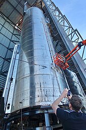 Musk standing before a Starship rocket, capturing an image with his phone