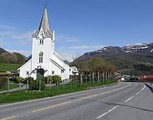 Foto einer Straße und einer weiß gestrichenen Holzkirche in bergiger Landschaft