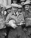 Formby in army uniform, playing his ukulele, surrounded by soldiers