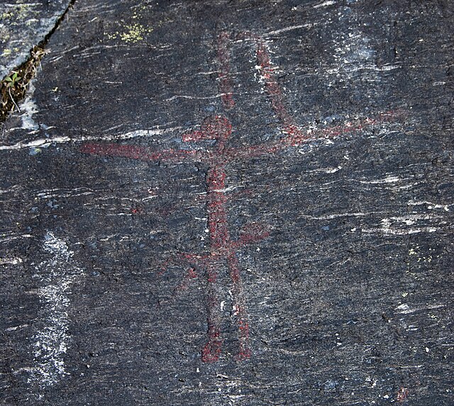 Human-like figure with a bird-like head and objects sticking out from its body.