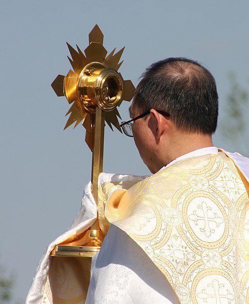 The Blessed Sacrament in a monstrance carried in a procession by a priest wearing a humeral veil