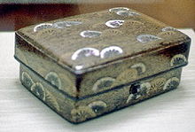 Caja con diseño de ruedas en oro y blanco sobre fondo negro.