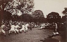 Foto de duas equipes de vários homens puxando uma corda de cada lado no meio de um campo.